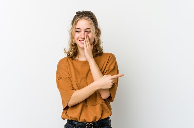 Jovem mulher caucasiana em branco backrgound dizendo uma fofoca, apontando para o lado relatando algo.