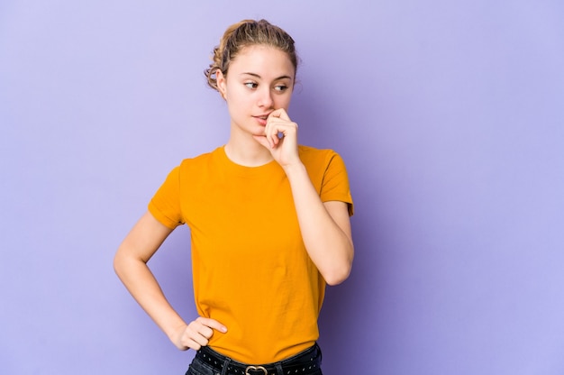 Jovem mulher caucasiana em fundo roxo relaxado pensando em algo olhando para um espaço de cópia.