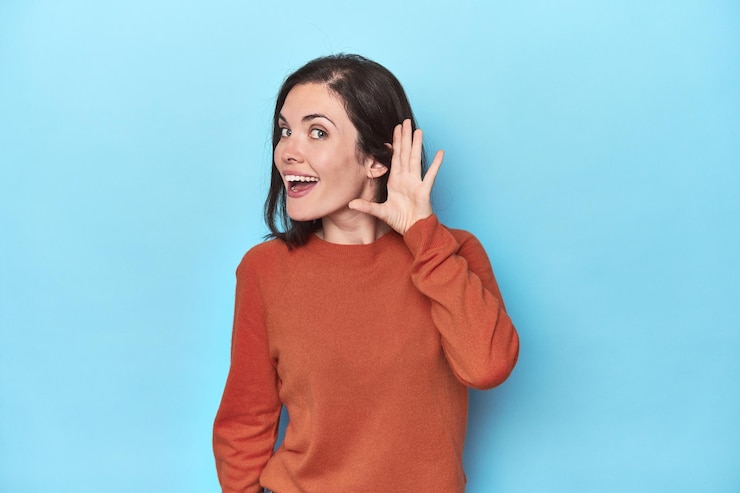Foto jovem mulher caucasiana em pano de fundo azul tentando ouvir uma fofoca