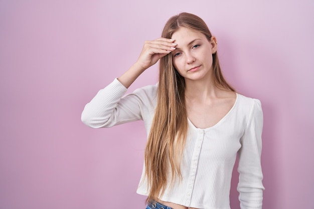 Jovem mulher caucasiana em pé sobre fundo rosa preocupada e estressada com um problema com a mão na testa, nervosa e ansiosa por crise