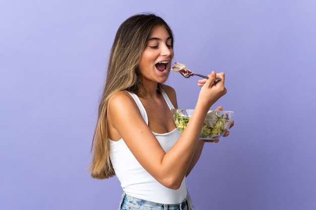 Jovem mulher caucasiana em roxo segurando uma tigela de salada com uma expressão feliz