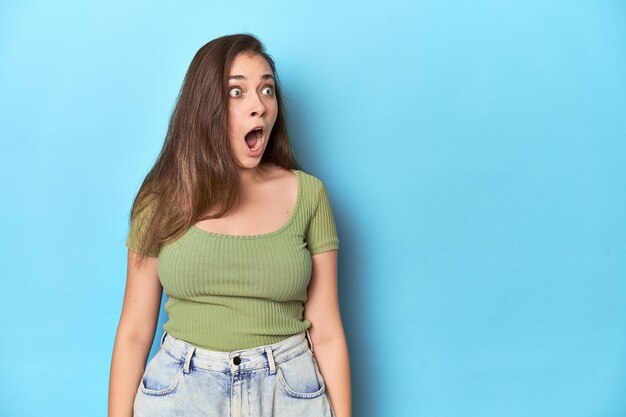 Jovem mulher caucasiana em um top verde em um fundo azul sendo chocado