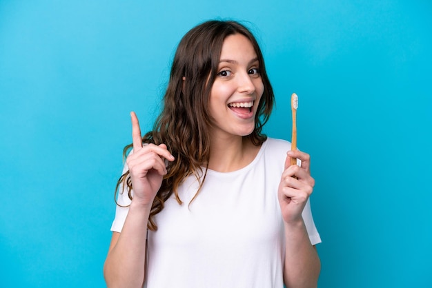 Jovem mulher caucasiana escovando dentes isolados em um fundo azul apontando para uma ótima ideia