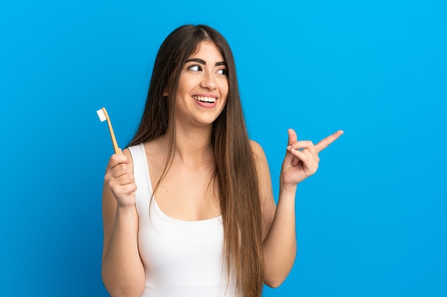 Jovem mulher caucasiana, escovando dentes isolados em um fundo azul com a intenção de perceber a solução enquanto levanta um dedo