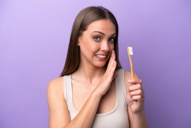 Jovem mulher caucasiana escovando os dentes isolados em fundo roxo sussurrando algo