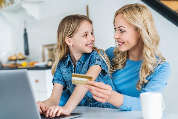 Jovem mulher caucasiana fazendo compras on-line usando cartão de crédito com a filha em casa