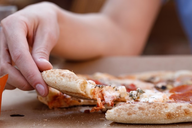 Jovem mulher caucasiana feliz sentada à mesa comendo pizza recém-assada e bebendo fresco no café ao ar livre em um dia claro e ensolarado de verão