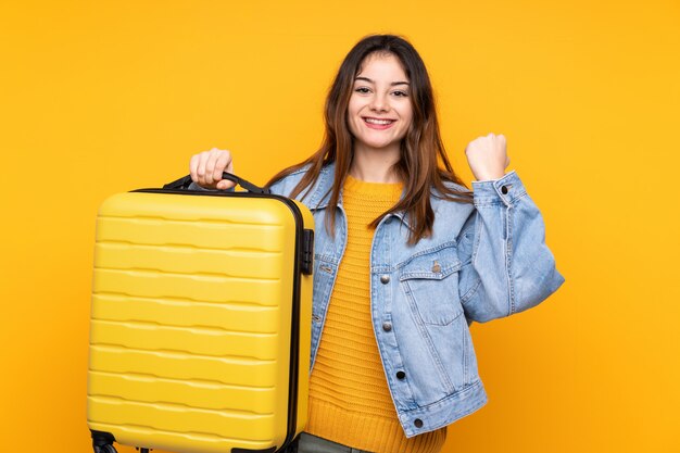 Jovem mulher caucasiana isolada em amarelo em férias com mala de viagem