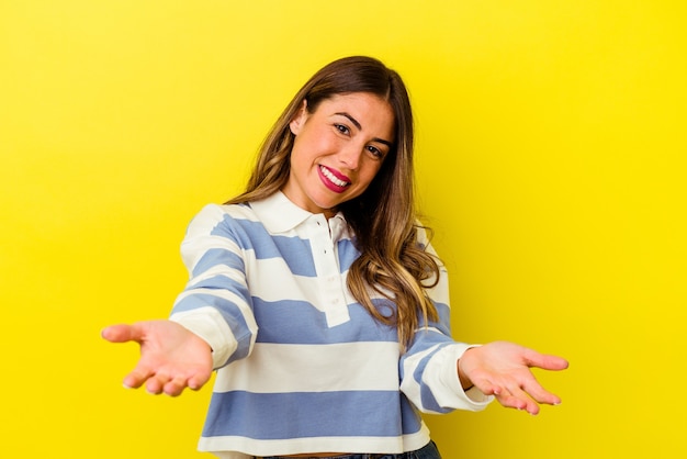 Jovem mulher caucasiana isolada em amarelo, mostrando uma expressão de boas-vindas.