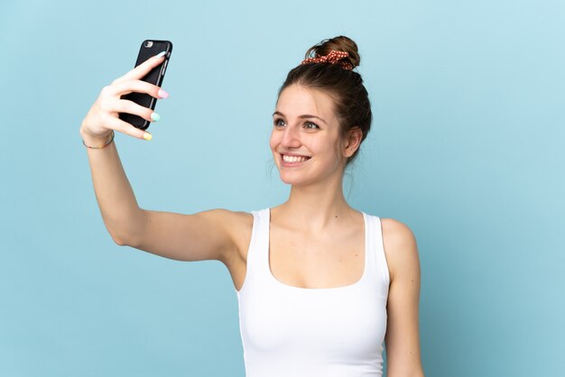 Jovem mulher caucasiana isolada em azul, fazendo um selfie