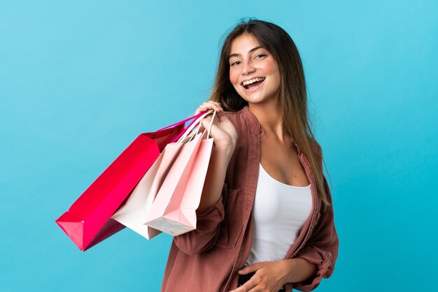 Jovem mulher caucasiana isolada em azul segurando sacolas de compras e sorrindo