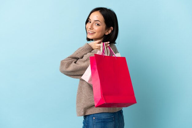 Jovem mulher caucasiana isolada em azul segurando sacolas de compras e sorrindo