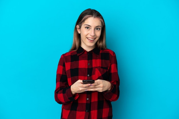 Foto jovem mulher caucasiana isolada em azul surpresa e enviando uma mensagem