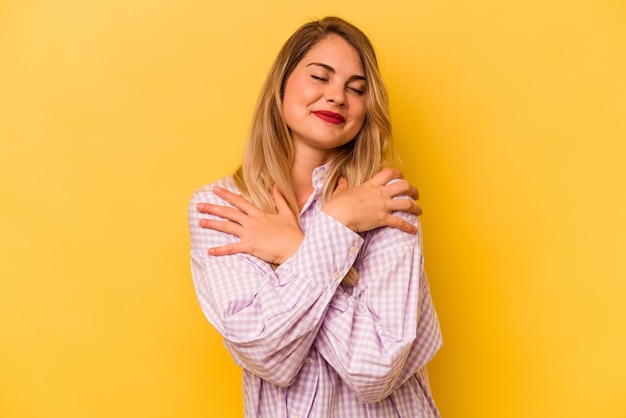 Foto jovem mulher caucasiana isolada em fundo amarelo abraça sorrindo despreocupada e feliz