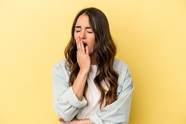 Jovem mulher caucasiana isolada em fundo amarelo bocejando mostrando um gesto cansado cobrindo a boca com a mão