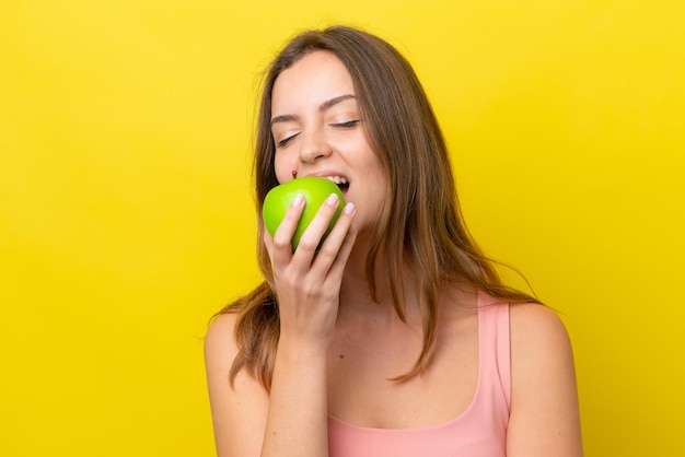 Jovem mulher caucasiana isolada em fundo amarelo comendo uma maçã