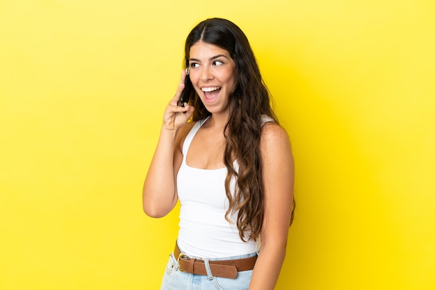 Jovem mulher caucasiana isolada em fundo amarelo, conversando com alguém ao telefone celular