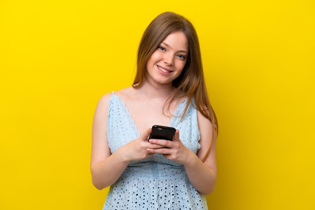 Jovem mulher caucasiana isolada em fundo amarelo enviando uma mensagem com o celular