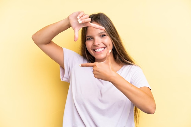 Jovem mulher caucasiana isolada em fundo amarelo, focando o símbolo de enquadramento do rosto