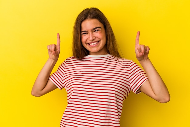 Jovem mulher caucasiana isolada em fundo amarelo indica com os dois dedos anteriores mostrando um espaço em branco.