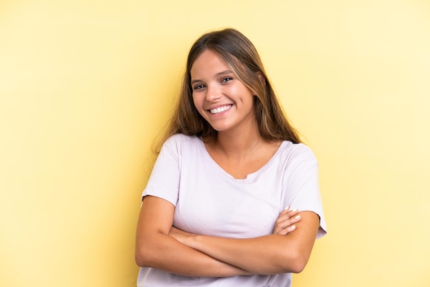 Jovem mulher caucasiana isolada em fundo amarelo, mantendo os braços cruzados na posição frontal