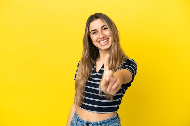 Jovem mulher caucasiana isolada em fundo amarelo, mostrando e levantando um dedo