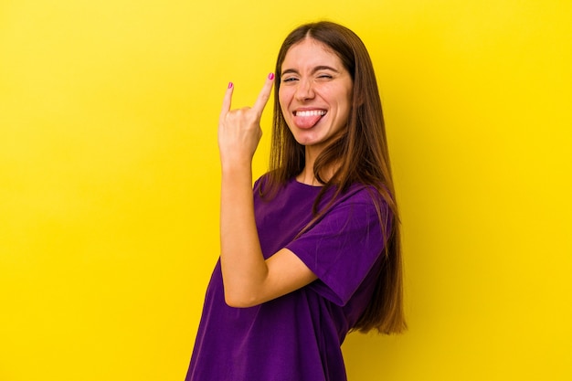 Jovem mulher caucasiana isolada em fundo amarelo mostrando gesto de pedra com os dedos