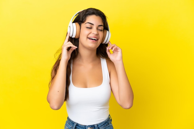 Jovem mulher caucasiana isolada em fundo amarelo ouvindo música e cantando