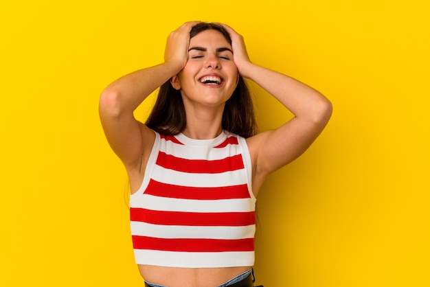 Foto jovem mulher caucasiana isolada em fundo amarelo ri com alegria, mantendo as mãos na cabeça. conceito de felicidade.