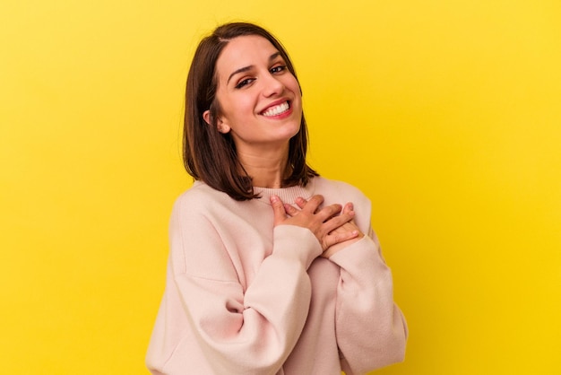 Foto jovem mulher caucasiana isolada em fundo amarelo tem expressão amigável pressionando a palma da mão no peito conceito de amor