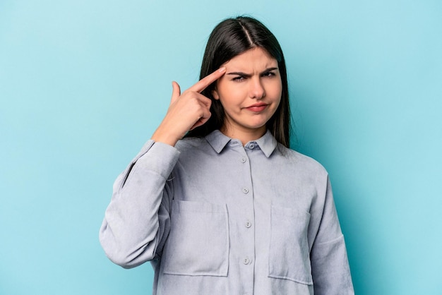 Jovem mulher caucasiana isolada em fundo azul apontando o templo com o dedo pensando focado em uma tarefa