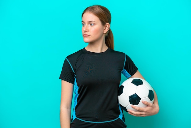 Jovem mulher caucasiana isolada em fundo azul com bola de futebol