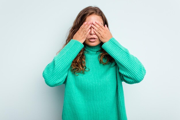 Foto jovem mulher caucasiana isolada em fundo azul com medo cobrindo os olhos com as mãos