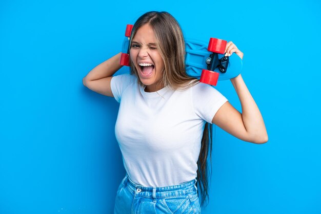 Jovem mulher caucasiana isolada em fundo azul com um skate