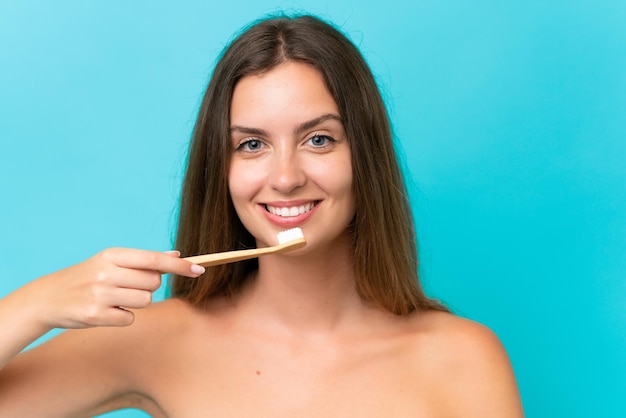 Jovem mulher caucasiana isolada em fundo azul com uma escova de dentes e expressão feliz