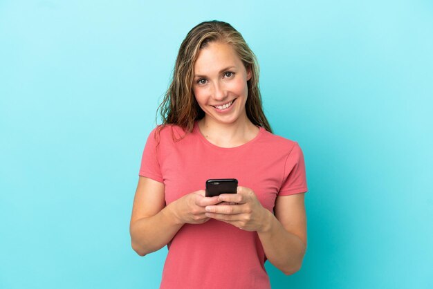 Jovem mulher caucasiana isolada em fundo azul enviando uma mensagem com o celular