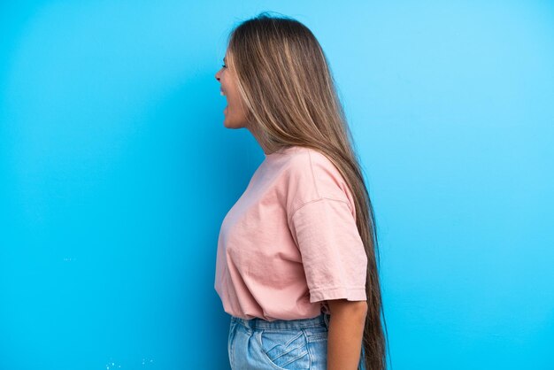 Jovem mulher caucasiana isolada em fundo azul rindo na posição lateral