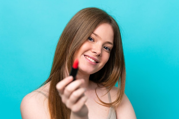 Jovem mulher caucasiana isolada em fundo azul segurando batom vermelho e oferecendo-o