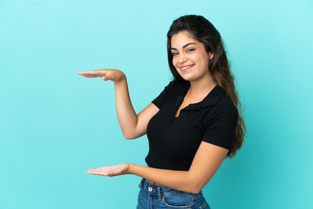 Jovem mulher caucasiana isolada em fundo azul segurando copyspace para inserir um anúncio