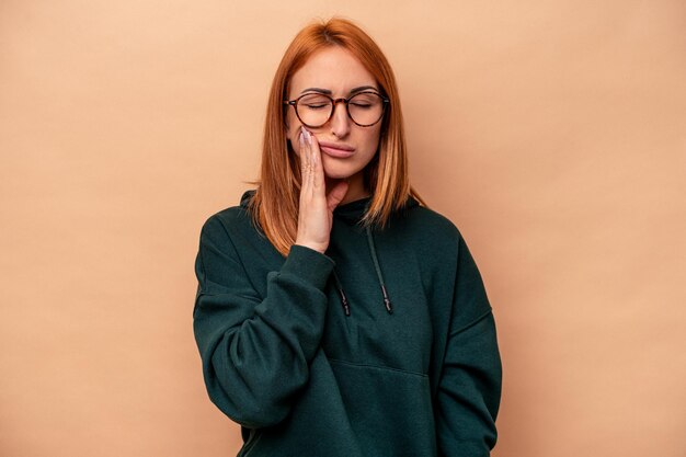 Jovem mulher caucasiana isolada em fundo bege com uma forte dor de dentes, dor molar.