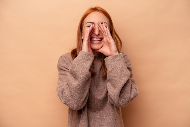 Jovem mulher caucasiana isolada em fundo bege, dizendo uma fofoca, apontando para o lado relatando algo.