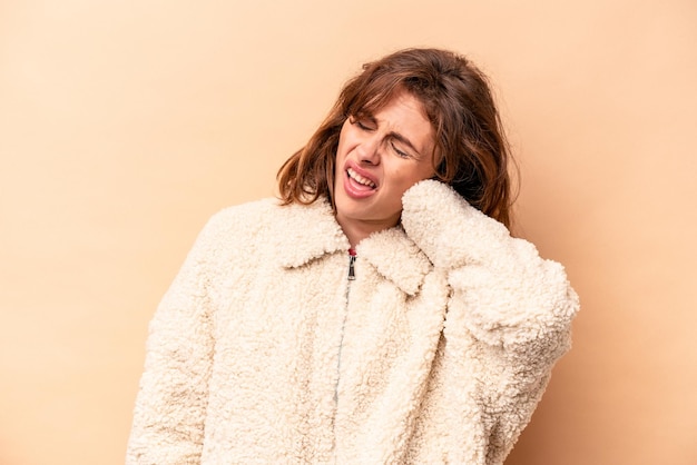 Foto jovem mulher caucasiana isolada em fundo bege, sofrendo dor no pescoço devido ao estilo de vida sedentário