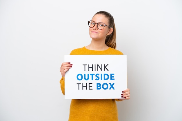 Jovem mulher caucasiana isolada em fundo branco segurando um cartaz com texto Think Outside The Box
