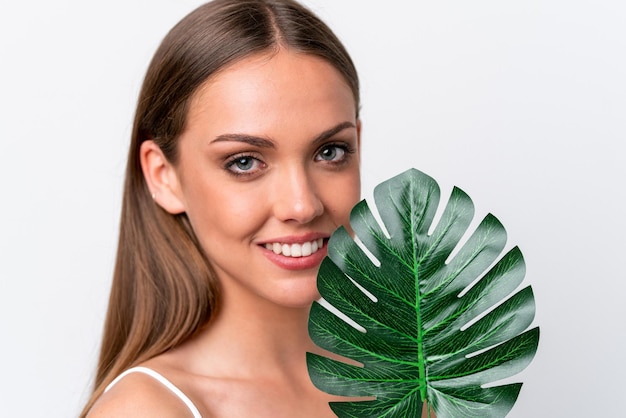 Jovem mulher caucasiana isolada em fundo branco segurando uma folha de palmeira com expressão feliz Feche o retrato