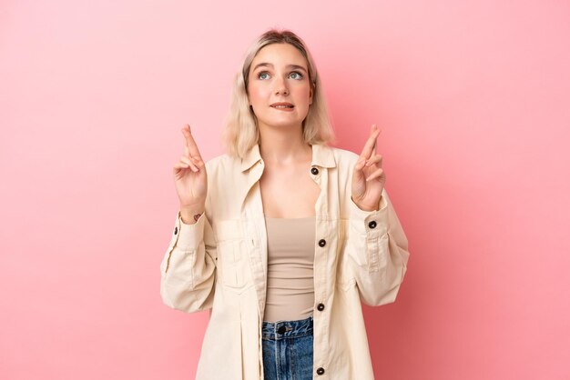 Jovem mulher caucasiana isolada em fundo rosa com dedos cruzando e desejando o melhor