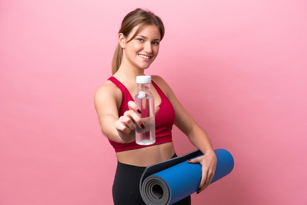 Jovem mulher caucasiana isolada em fundo rosa com garrafa de água esportiva e com um tapete