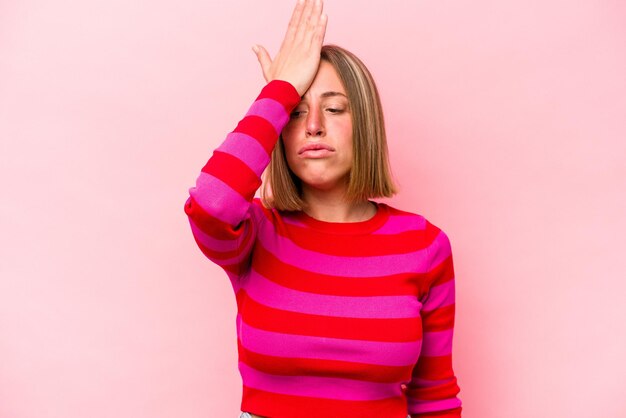 Jovem mulher caucasiana isolada em fundo rosa, esquecendo algo batendo na testa com a palma da mão e fechando os olhos