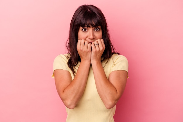 Jovem mulher caucasiana isolada em fundo rosa, roendo as unhas, nervosa e muito ansiosa.