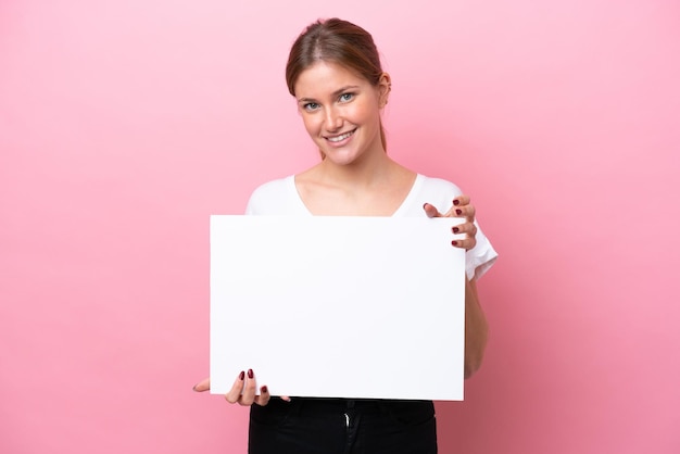 Jovem mulher caucasiana isolada em fundo rosa segurando um cartaz vazio com expressão feliz