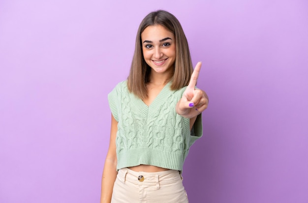 Jovem mulher caucasiana isolada em fundo roxo mostrando e levantando um dedo